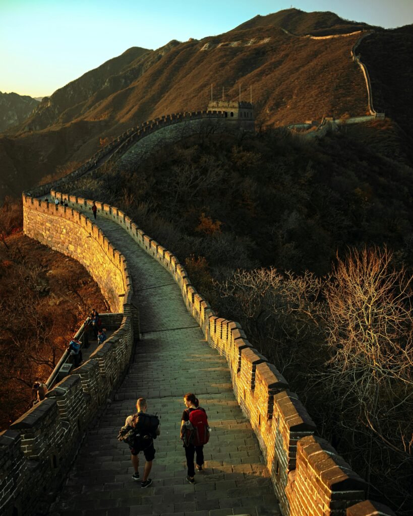 Tourists walking along the Great Wall of China at sunset with mountainous backdrop.