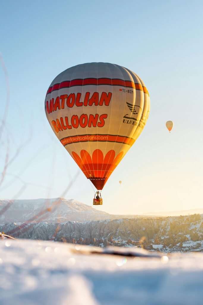 Hot air balloon floating above snowy Cappadocia landscape during sunrise in winter.