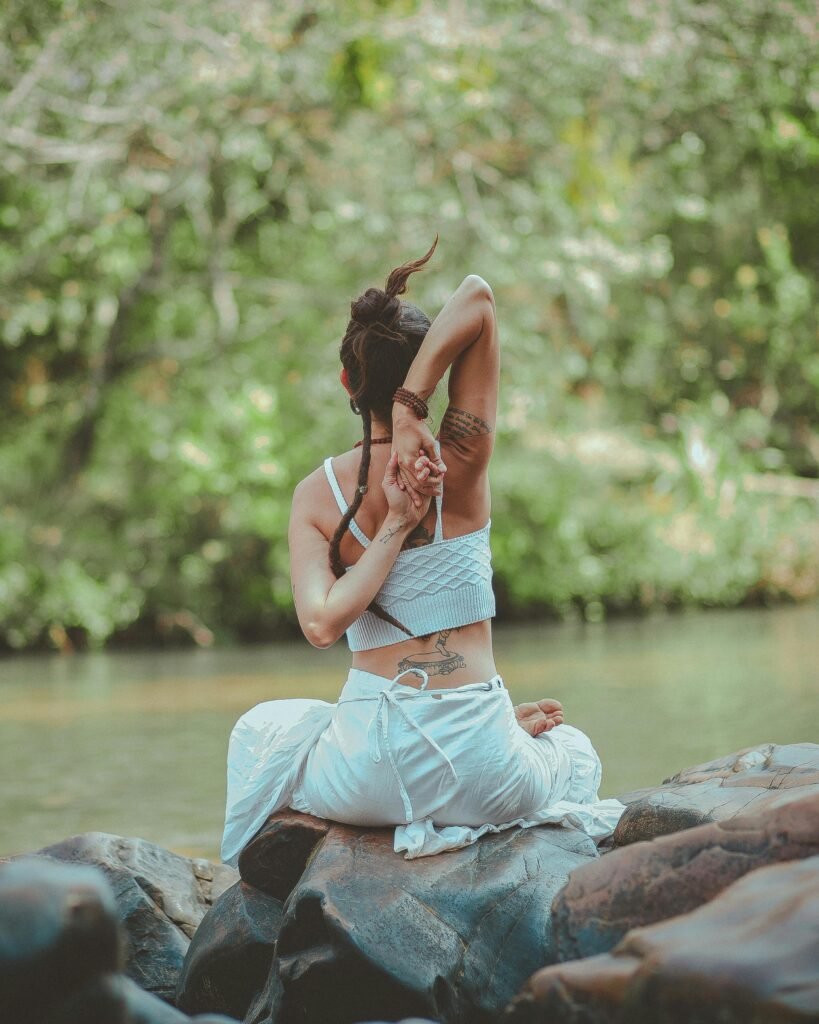 A woman in a yoga pose by a calm river, surrounded by nature, embodying peace and tranquility.