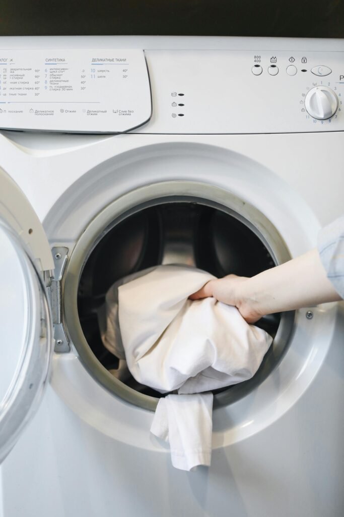 Close-up of a person's hand putting laundry into a front-loading washing machine.