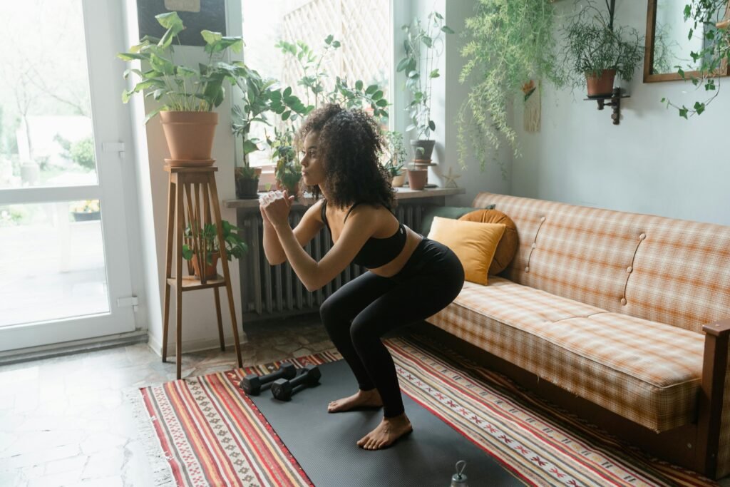 Woman in active wear doing squats on a yoga mat in a cozy indoor setting with plants and natural light.