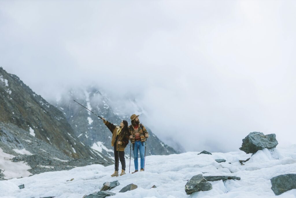 Couple exploring snowy mountains with hiking poles on a foggy day, enjoying the adventure.