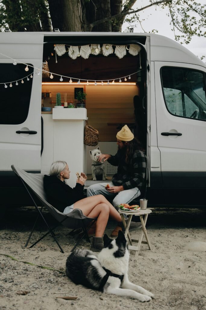 Cozy outdoor gathering by a campervan, featuring two people and their dogs enjoying a peaceful day.