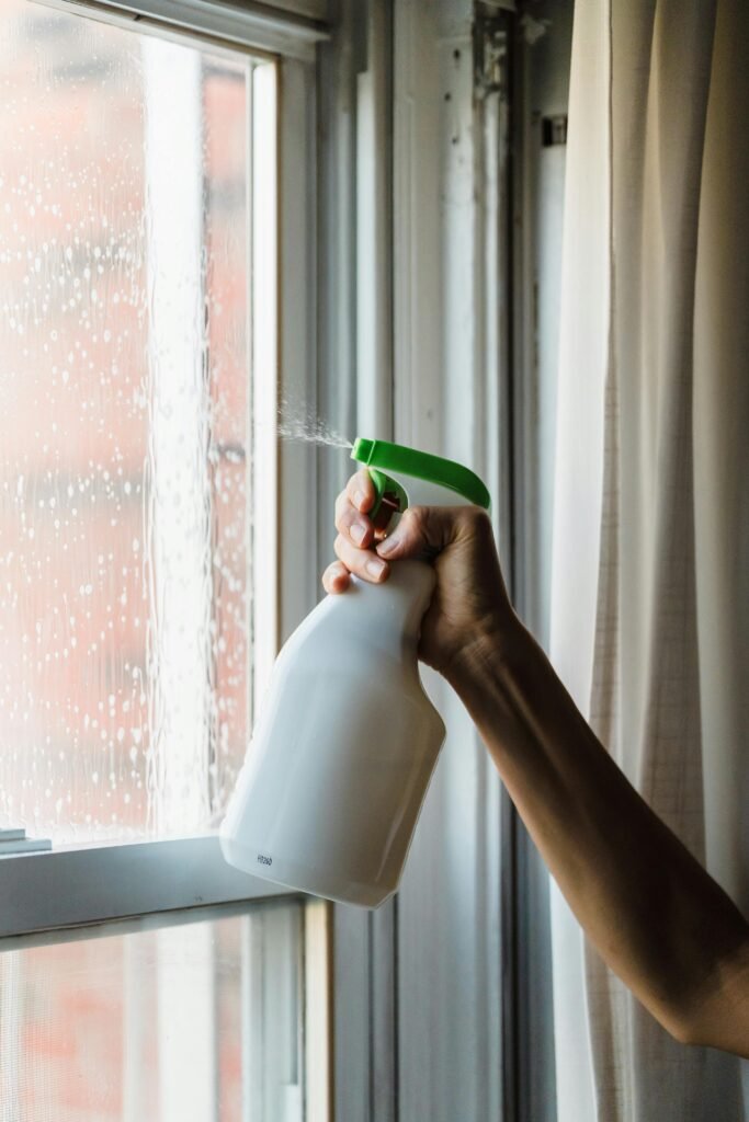 Close-up of a hand using a spray bottle to clean a glass window, emphasizing cleanliness.