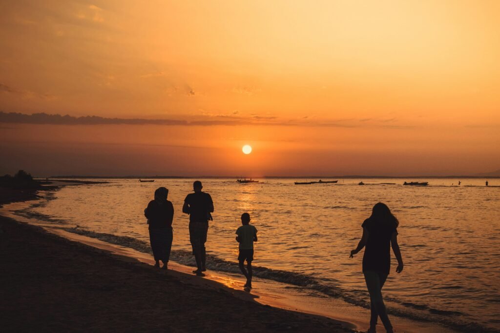 A family walking along Mandra beach, Greece, silhouetted against a stunning sunset.