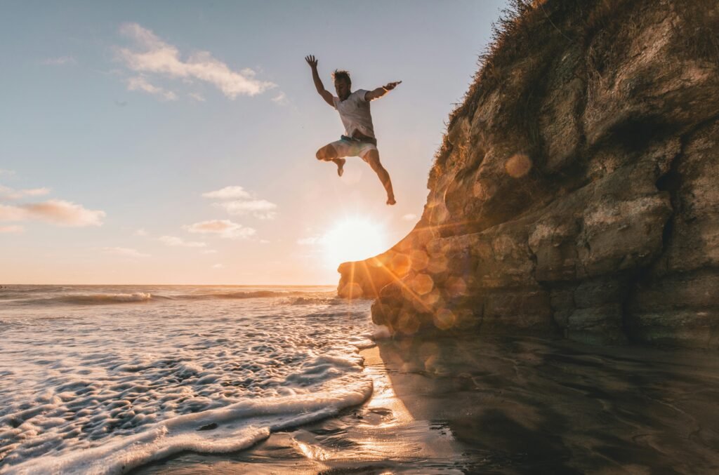 A man jumps off a cliff at sunset in Encinitas, California, capturing a moment of adventure by the sea.