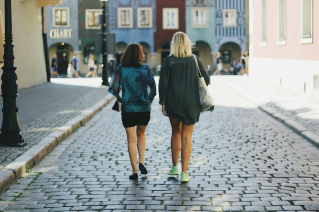 Two women enjoying a leisurely walk on a sunny cobblestone street.