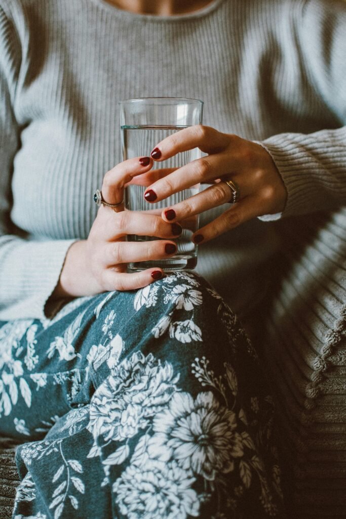 Up-close shot of a woman holding a water glass with floral pants indoors.