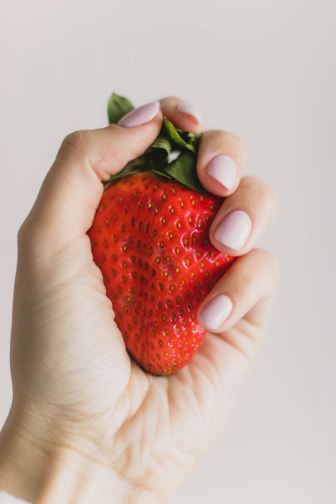 A close-up image of a hand grasping a ripe red strawberry, showcasing freshness and color.