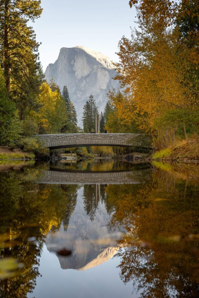 Beautiful autumn scene with a bridge and Half Dome at Yosemite National Park, reflecting in a calm river.