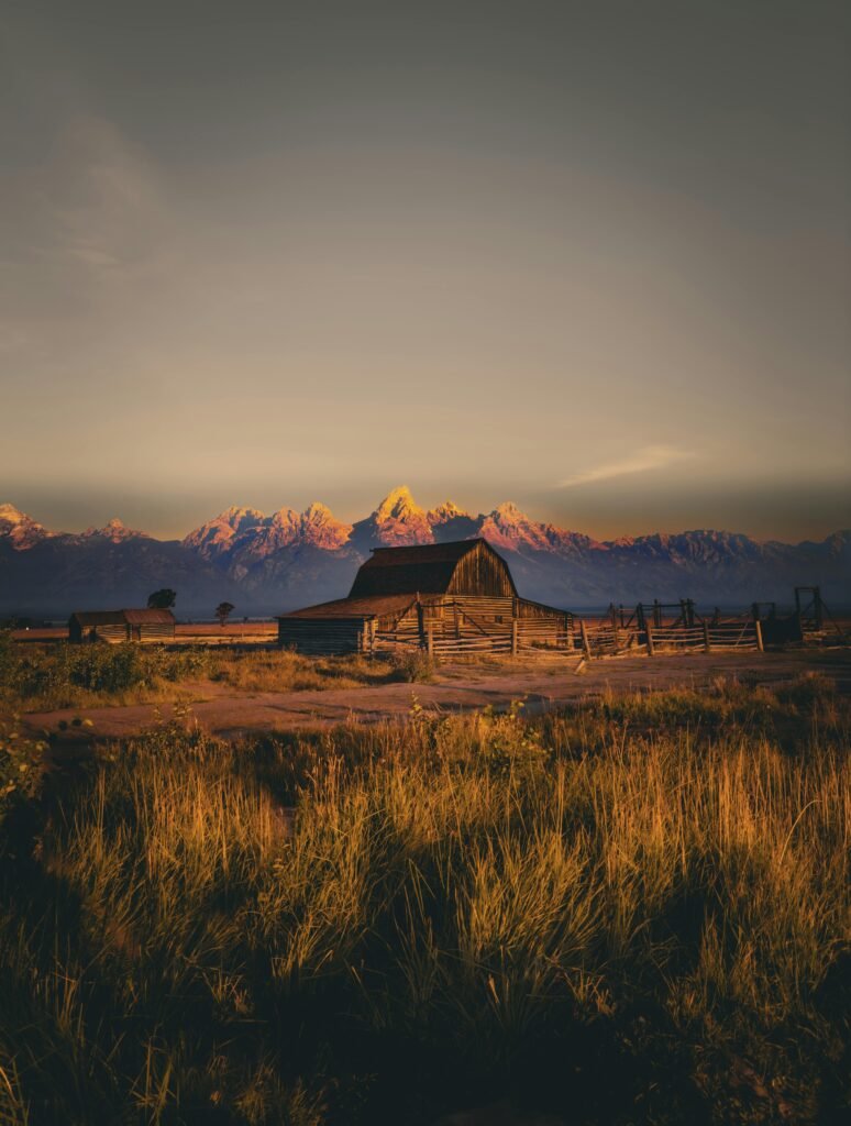 Rustic Wyoming barn set against a stunning mountain backdrop at sunset.