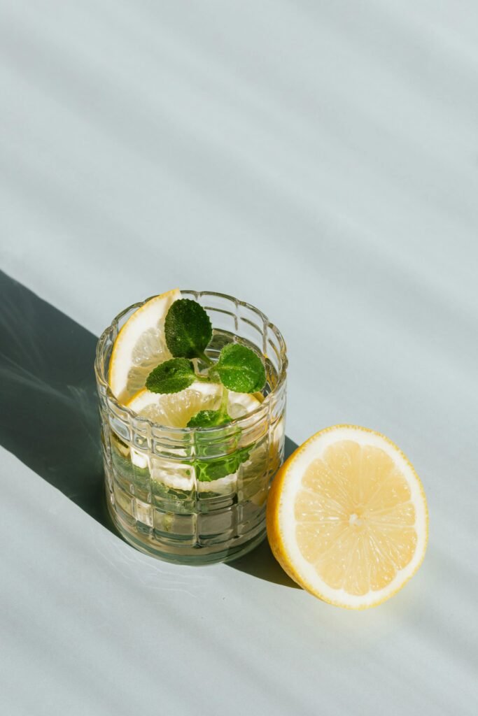 Icy lemon mint drink in glass, half lemon beside, casting cool shadows on table.