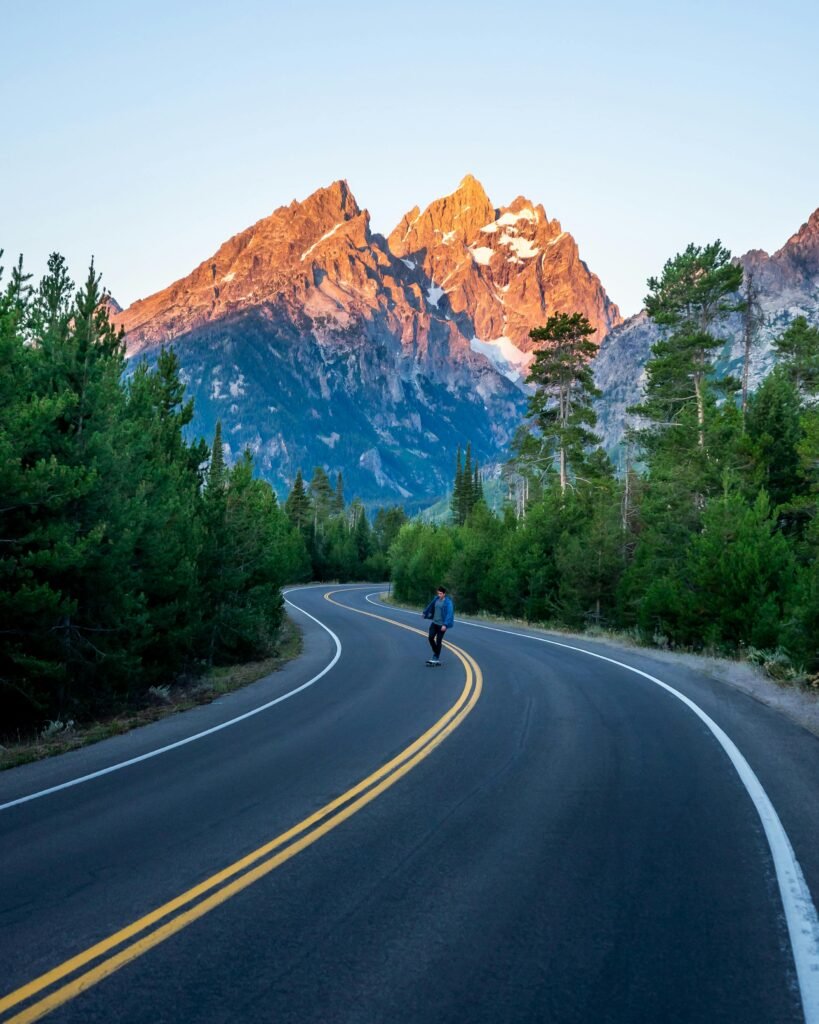 A cyclist on a winding road leads to the majestic Grand Teton mountains, WY.