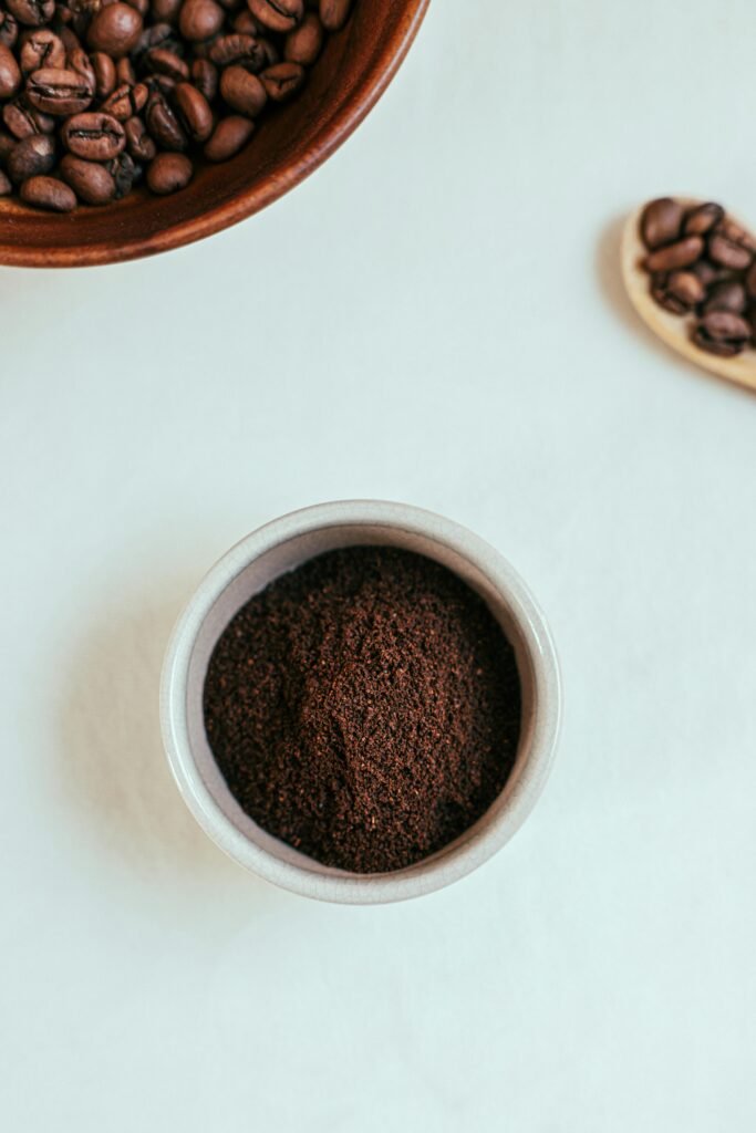 Top view of aromatic roasted coffee beans and ground coffee in bowls on a white background.