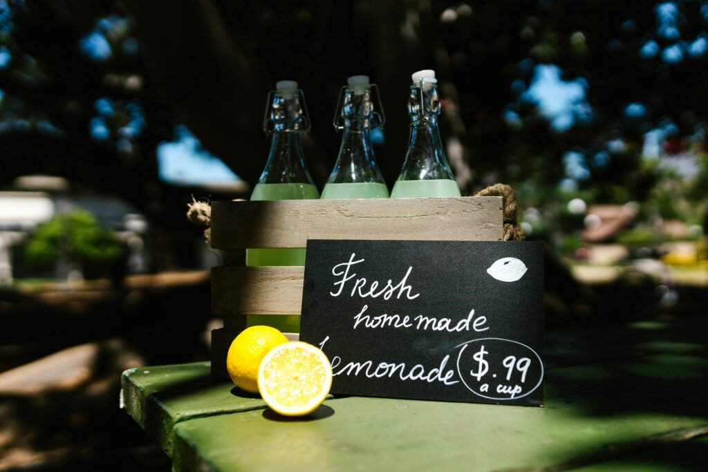 Crate of glass bottles with lemonade on outdoor table, priced at $0.99 a cup.