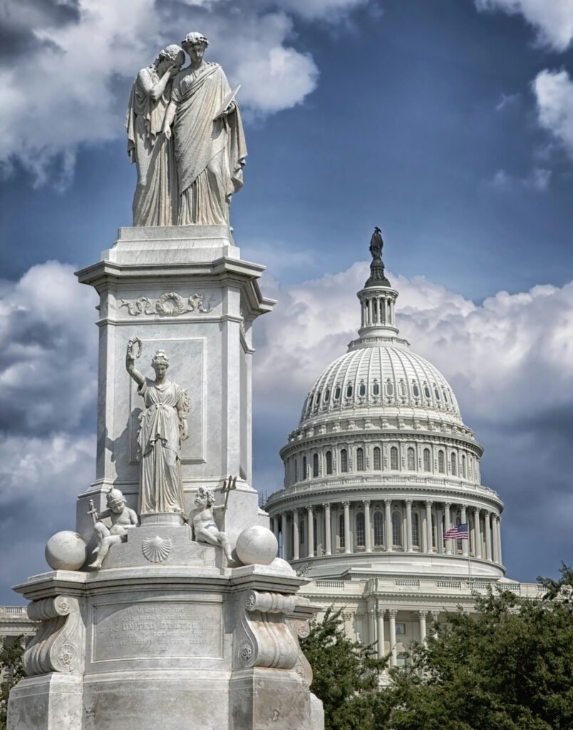 US Capitol building with Peace Monument statue under dramatic clouds.