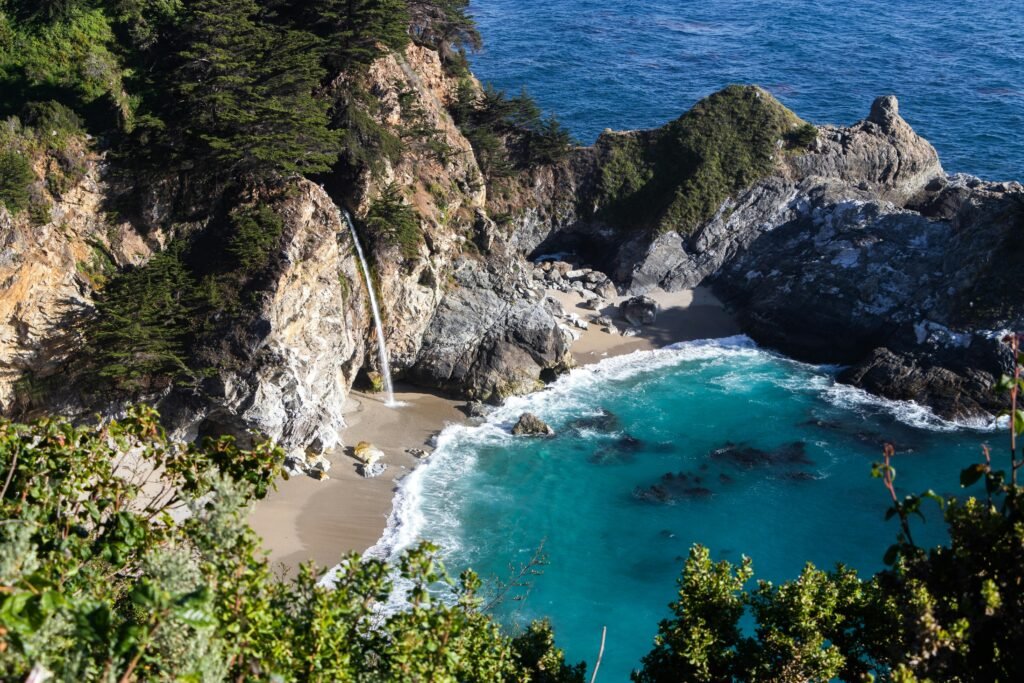 From above breathtaking scenery of turquoise lagoon surrounded by rocky cliffs with waterfall on sunny day